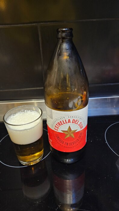 Flaska och glas av öl "Estrella del Sur" på ett köksbord.