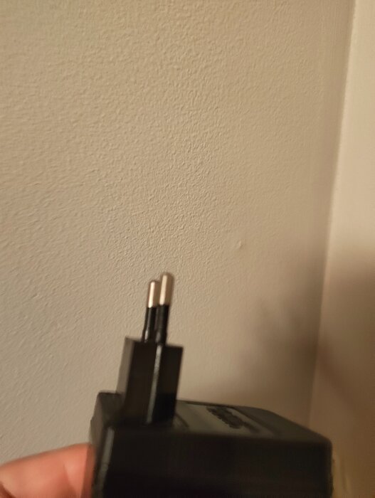 Dubbelisolerad kontaktplugg, svart, mot ljus vägg. Liknar de som används för LED-slangar och adventsbelysning, kopplad till jordfelsproblematik.