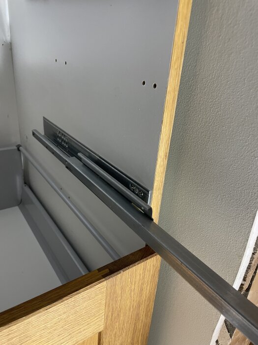 Köksskåp med utdraget träfronthörn och synlig metallspåra för lådan utan soft-close funktion.