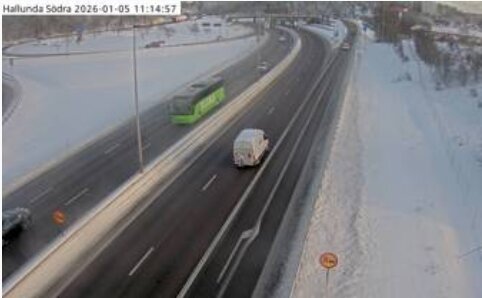 En motorväg med snötäckt omgivning, där en grön buss och en vit skåpbil kör i varsin riktning.