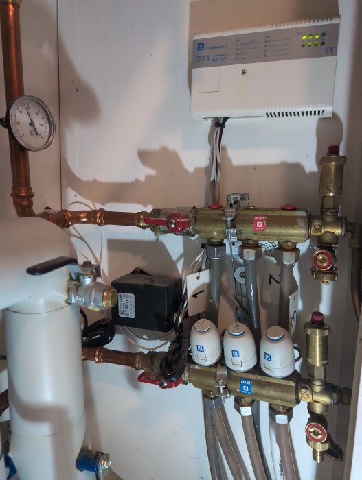 Pump- och rörsystem för golvvärme med flera ventiler, mätare och styrbox, del av fjärrvärmesystem.