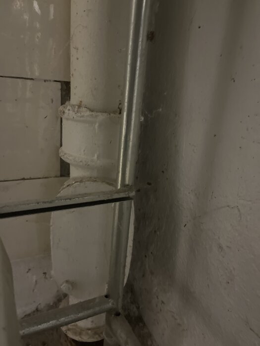 Överdimensionerat avloppsrör under diskbänken med metallram i närbild, fokus på rörstorlek och installation.