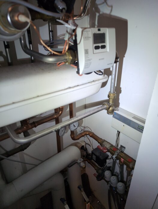 VVS-system med rör, ventiler och mätare, samt en regulator monterad på väggen.