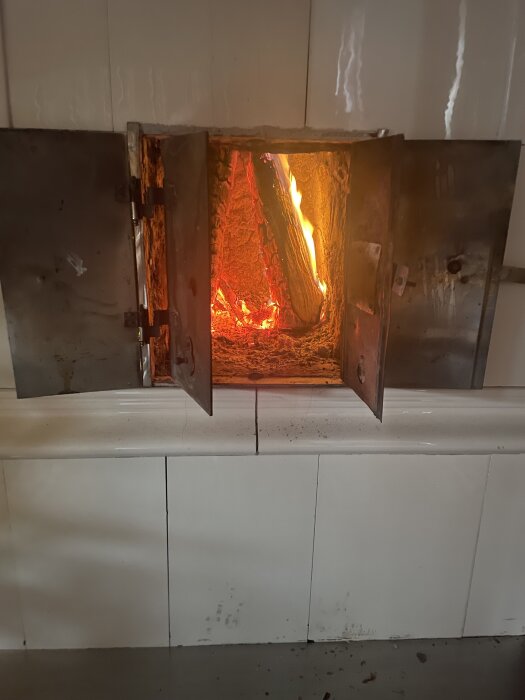 En brinnande vedklabbe inuti en öppen kakelugn, med eldslågor och glödande kol.