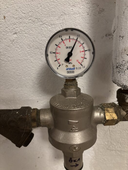 Manometer visar vattentryck nära 8 bar, del av ett värmesystem med tryckregulator och rör, potentiellt problem med pumputrustning.