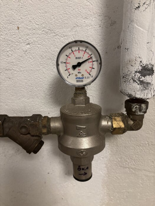 Manometer visar vattentryck i ledning, cirka 0,2 MPa (2 bar), med rostig röranslutning och text "öka" på tryckregulatorn i källarutrymme.
