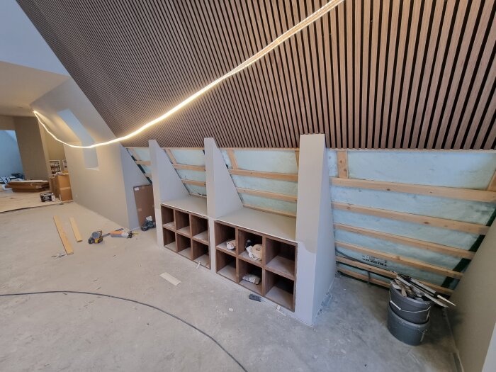 Byggarbetsplats för kök med oskruvade skåp, träpanel på väggen och verktyg på golvet, insidan av ett hus under renovering.