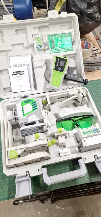 Förpackning med 360° laserverktyg, mottagare och tillbehör i en plastlåda på ett grönt arbetsbord.