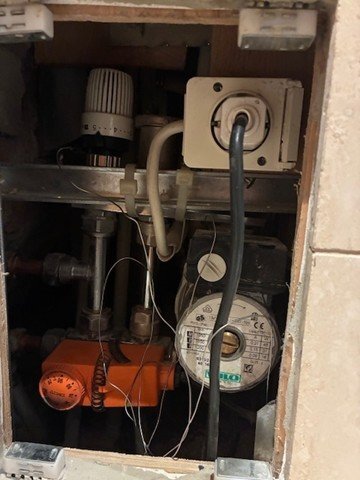 Vattenburet värmesystem i badrum med två termostater och cirkulationspump, varma rör förutom de under orange termostat.