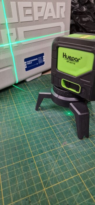 Grön Huepar laser med stativ projicerar en linje över en verktygslåda och en skärmatta.