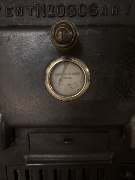 Termometer från Thermia-Verken Arvika på en äldre ugn eller panna, nummer 0306, med vred ovanför och ventilationslucka nedtill.