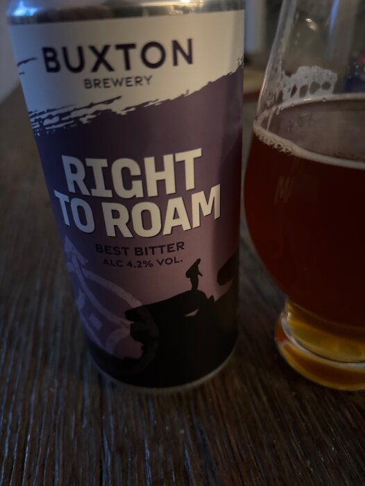 En burk Buxton Brewery "Right to Roam" Best Bitter och ett glas med samma öl på ett träbord.