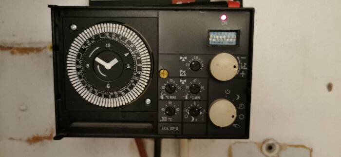 Danfoss ECL 3310 fjärrvärmecentral från 1995 med flera reglage och en analog timer, markerad inställning med gul pil.