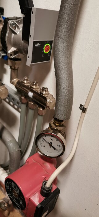 Fjärrvärmecentral med Danfoss ECL 3310, rör, röd pump och termometer som visar temperatur i grader Celsius i en anläggning.