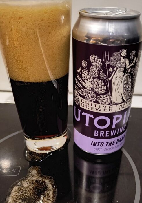 Burk och glas med mörk stoutöl på en svart spishäll. Etiketten på burken har en illustration med humle och en kvinna.