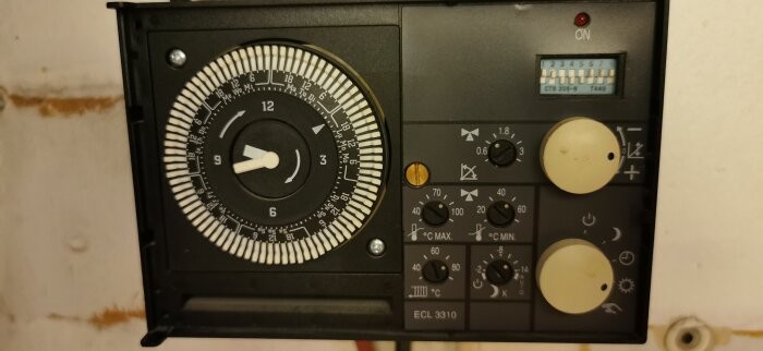 Termostat med urtavla och inställningsvred, märkt ECL 3310, med vit knapp och indikatorer för temperaturkontroll och tidsinställning.