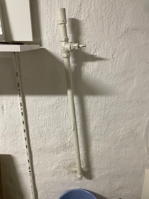 Rörledning med avstängningsventil på vitmålad källarvägg.
