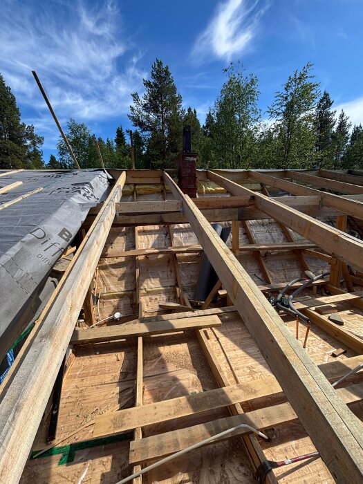 Rivning av tak visar träbalkar, isolering och en tegelstenad skorsten under blå himmel. Förberedelse för 340mm isolering.
