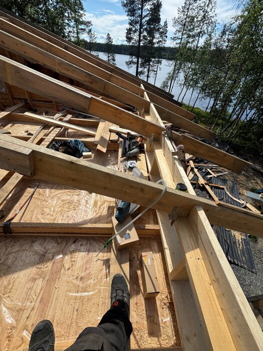 Rivning och byte av tak: Ny takkonstruktion byggs i trä med utsikt över sjö och skog. Förberedelse för installation av 340mm isolering.