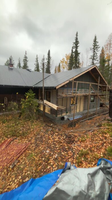 Hus under renovering med nytt tak och byggnadsställningar. Området är omgivet av träd och ger en vy av takhöjningen och isoleringsuppdateringen.