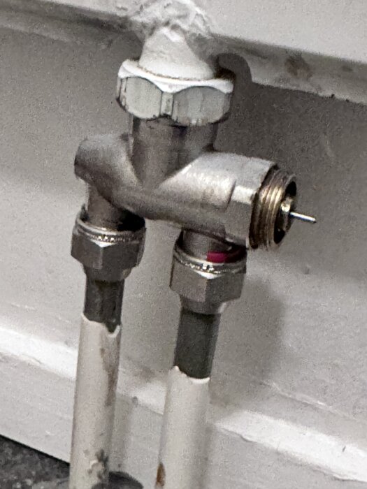 Radiatorventil med två rör och vit vägg i bakgrunden.