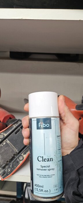 En hand håller en sprayburk med etiketten "Fibo Clean Special Remover Spray", placerad vid verktyg.