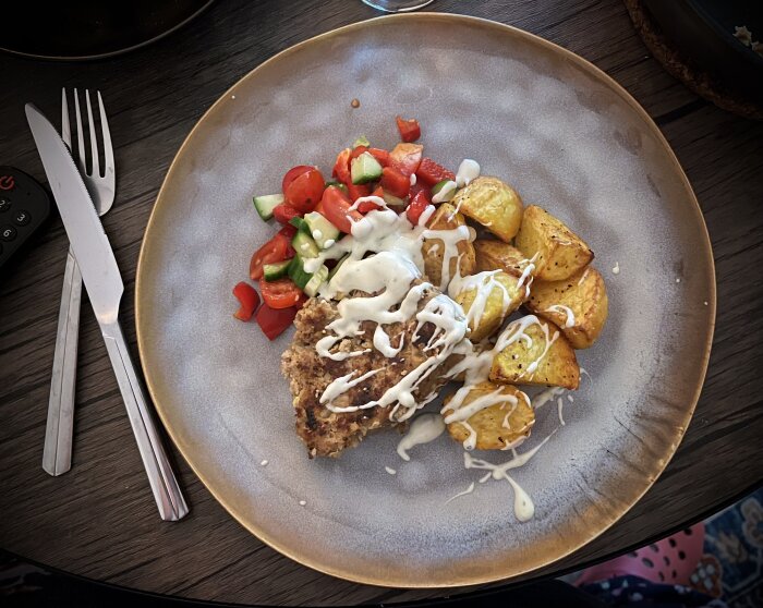 Tallrik med köttfärslimpa, ugnstekt potatis, sallad och gorgonzolasås på ett bord.