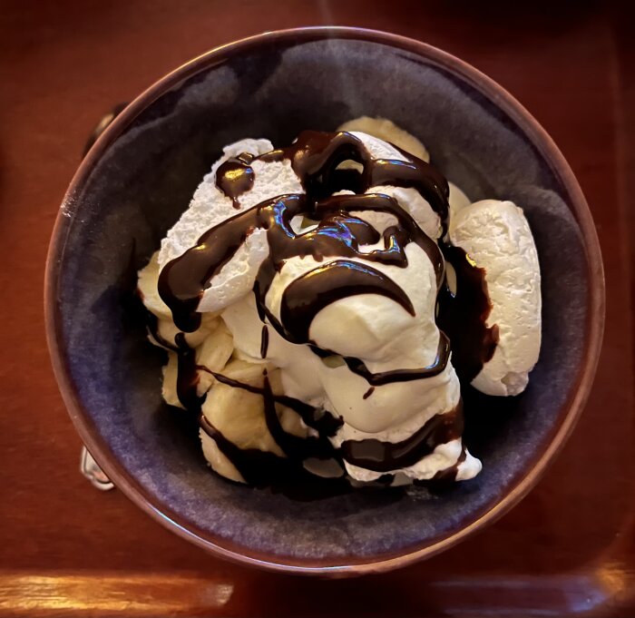Bowl med vaniljglass, banan, maräng och chokladsås, ser ut som en marängsviss dessert.