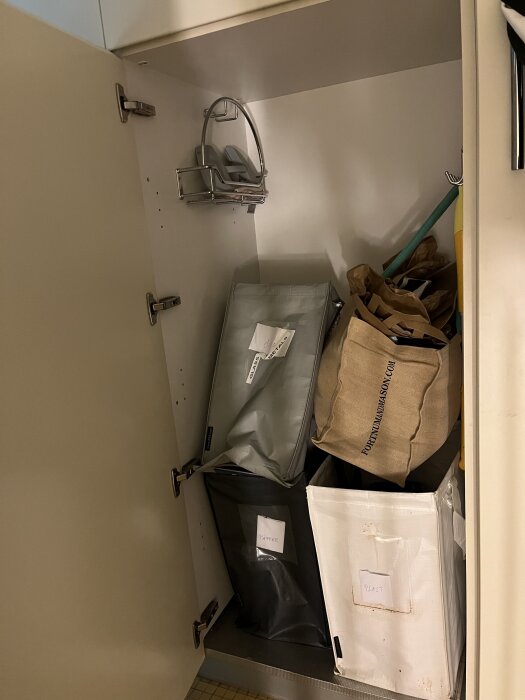 Öppet skåp med flera återvinningskärl märkta papper och plast, samt en tom hylla ovanför, i ett hemmabygge av tidigare ägare.