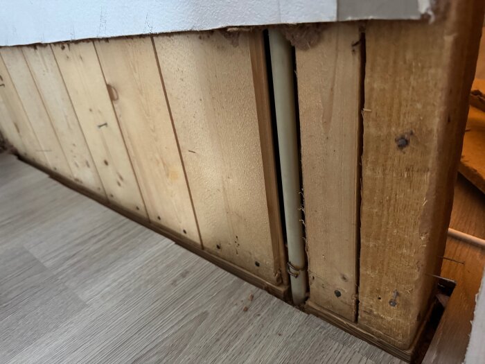 Luftspalt mellan träväggar med exponerat rör, visar rivet byggmaterial och trägolv.