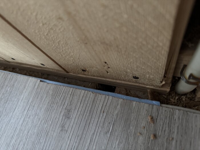 Luftspalt synlig mellan träpanel och golv efter rivning, med ett rör till höger.