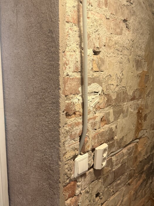 Rå tegelfasadvägg inomhus med oputsade delar, eluttag och kabelkanal synliga, potentiellt planerad för renovering och ommålning.