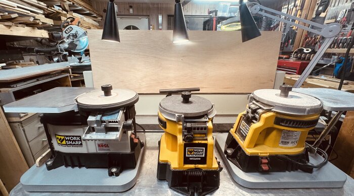 Tre slipmaskiner från Work Sharp, varav två är WS-2000-modeller, placerade på en arbetsbänk i en verkstad med belysning ovanför.