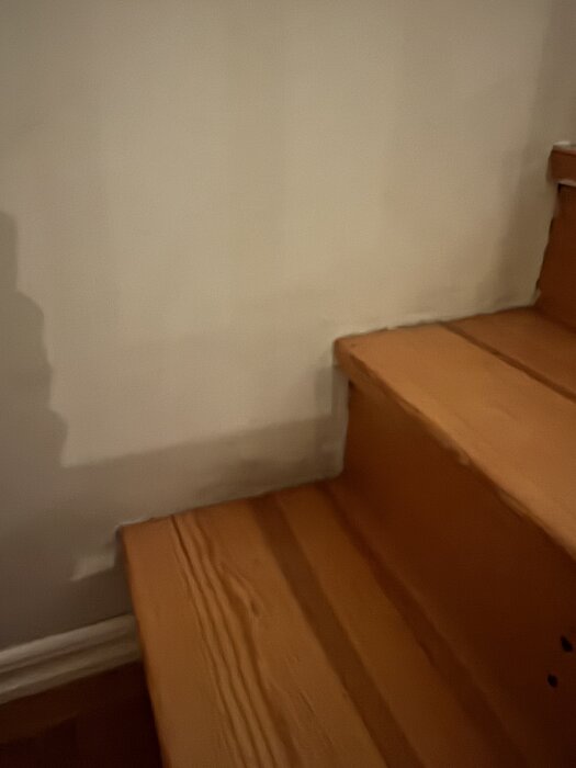 Trätrappa med synliga steg och vit vägg, fokus på området där tapeten ska skäras och vikas vid trappnosen.