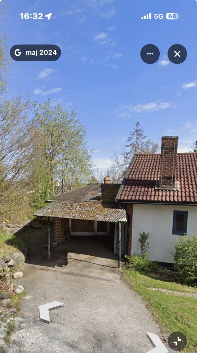 Hus med tegelpannetak, skorsten och en garageuppfart kantad av grönska och träd, under en klarblå himmel.