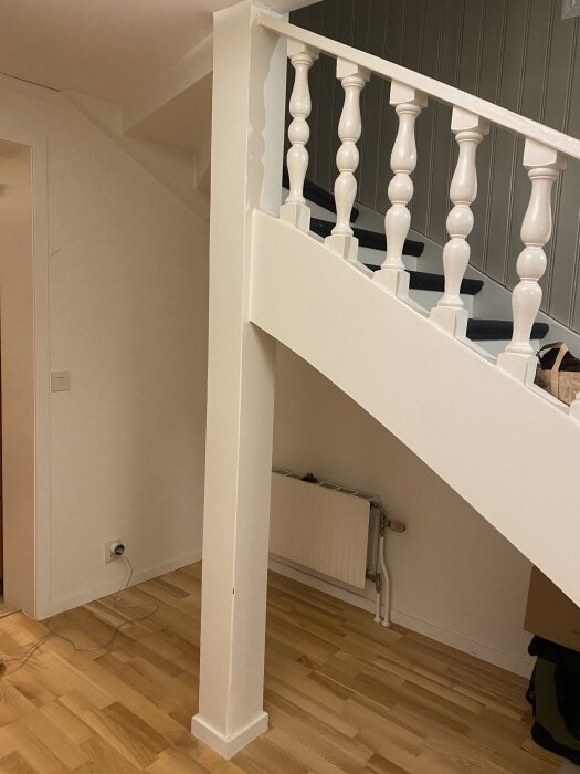 Vit trappa med räcke i ett hus, del av planlösningsprojekt. Träplankgolv, vit vägg, synlig radiator och elkabel vid golvsockel.
