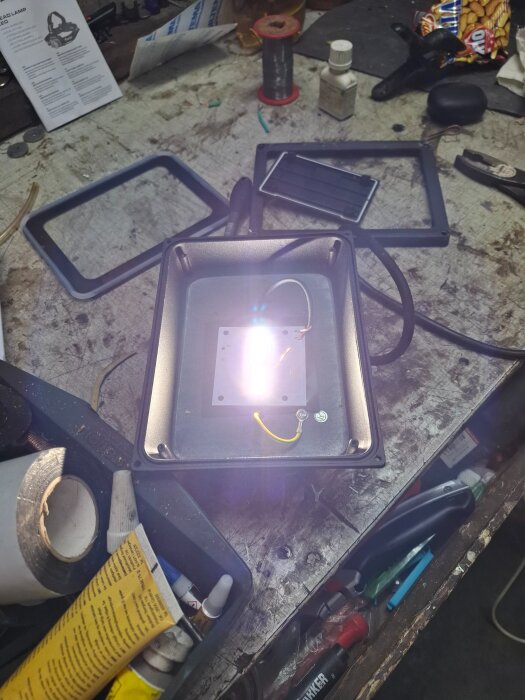 En halvt upplyst LED-armatur på ett arbetsbord med verktyg och material.