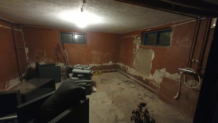 Renovering av källare med gamla väggar, viss del av väggen är exponerad. Rummet är sparsamt möblerat med några kuddar och möbler.