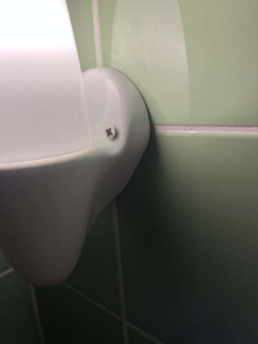 Armatur monterad på grön kakelvägg med synlig skruv, fastsatt i ett modernt våtrum.