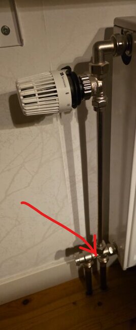 Radiatortermostat med kopparrör och anslutning indikerad av röd pil.
