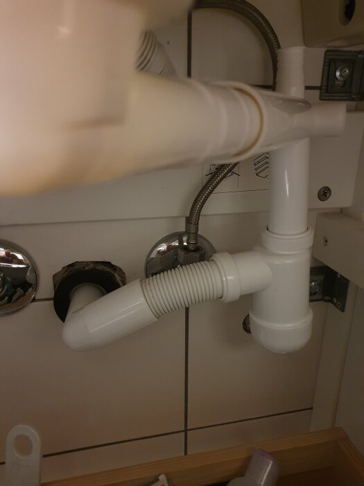 Under vasken syns ett rörsystem med vattenlås och avloppsrör installerat, fotograferat i en diskussionskontext om avloppsproblem.