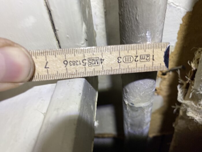 Person håller linjal vid ett grått rör i källartak för att mäta dimension, eventuellt 30 mm, för att köpa rätt koppling.