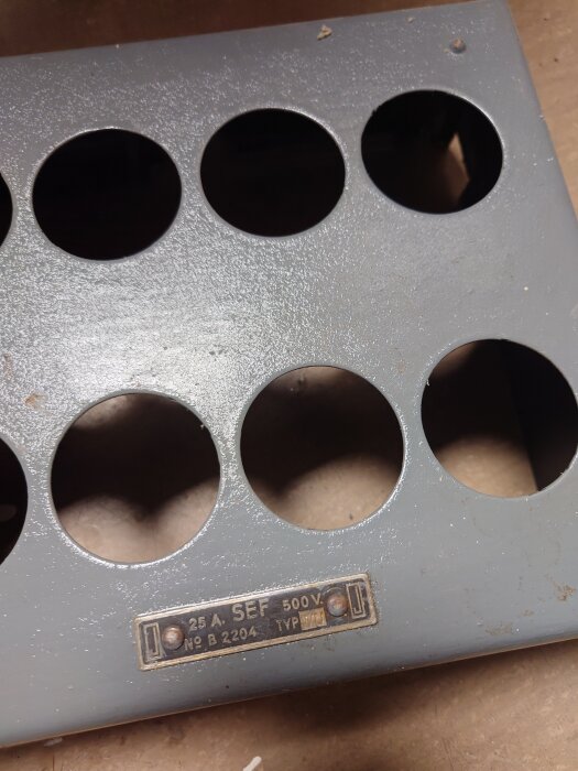 Grått metallock med runda hål och en skylt märkt "25 A SEF 500V, No B 2204".