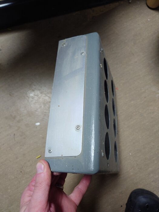 En metallplatta med flera runda utskärningar hålls i handen, vilket kan vara ett återanvänt lock till en elektrisk central.