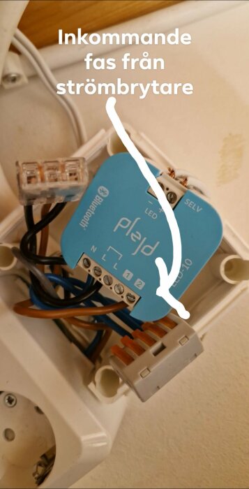 Bild på en Plejd-enhet med anslutna kablar, inkl. en markerad inkommande fas från strömbrytare. LED-indikator och Bluetooth-symbol synliga.