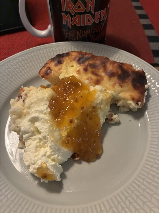 Ostkaka med sylt serverad på en tallrik, med en kaffemugg i bakgrunden.