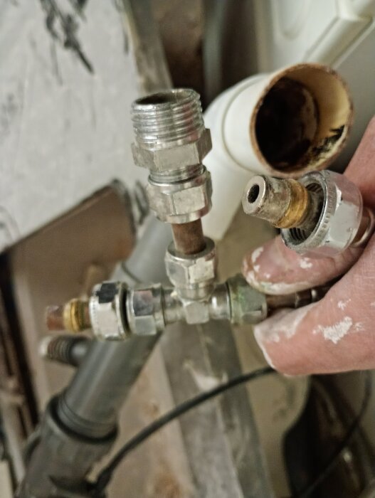 VVS-installation med kopparrör, tee-koppling och anslutningar för vattenledningar. En hand håller i rören, omgiven av olika VVS-komponenter.