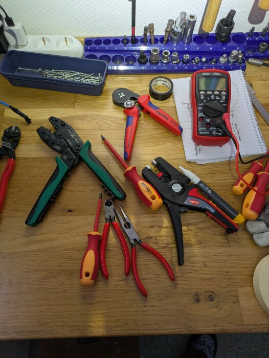 Verktyg på en arbetsbänk, inklusive crimptänger, mejsel, multimeter och en låda med skruvar.