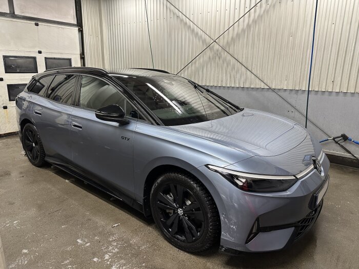 Grå bil i tvätthall, nypolerad och ren. Bilen står bredvid en tvätthallvägg med belysning ovanför. Våt golvyta efter tvätt.