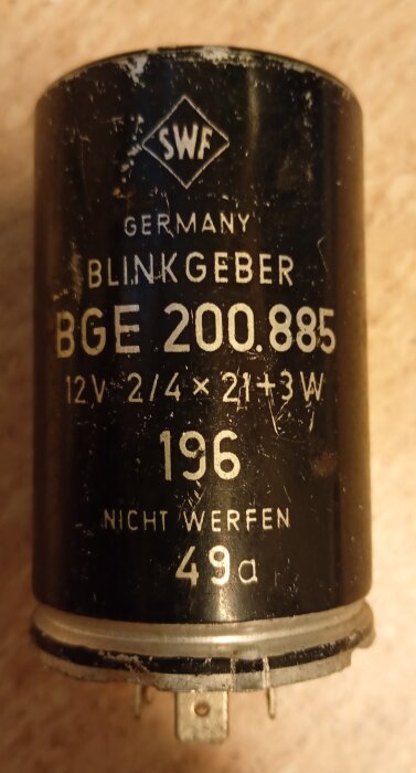 Svart cylinderformad blinkrelä från SWF, märkt med "Germany" och specifikationer som "BGE 200.885", "12V", och "Nicht Werfen".
